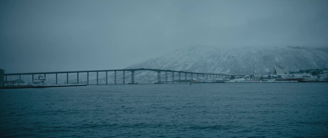 A bridge in the water leads to a snowy mountain