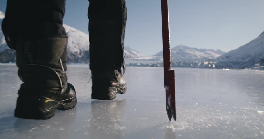 A person uses a pick as they walk across a lake covered in ice