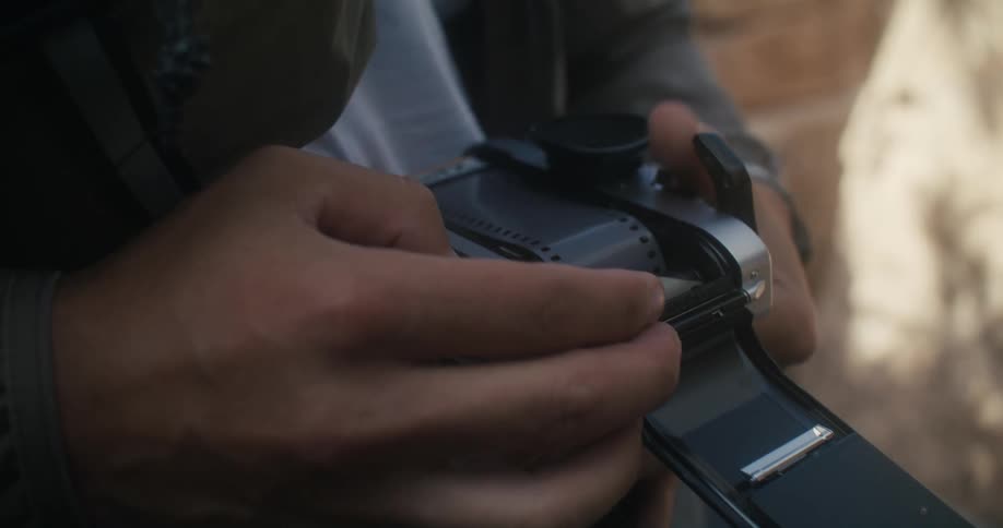 A man inserts a roll of film into a camera while outdoors