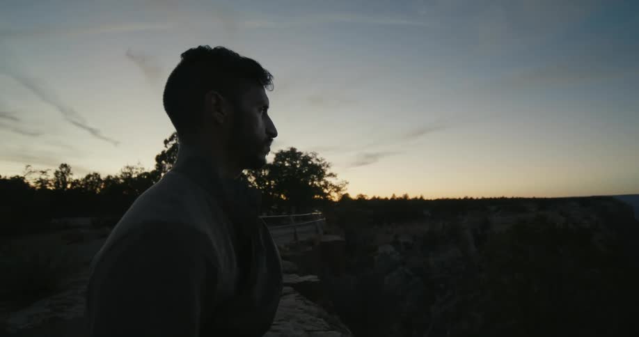Man stands on cliff overlooking ocean as afterglow turns sky red