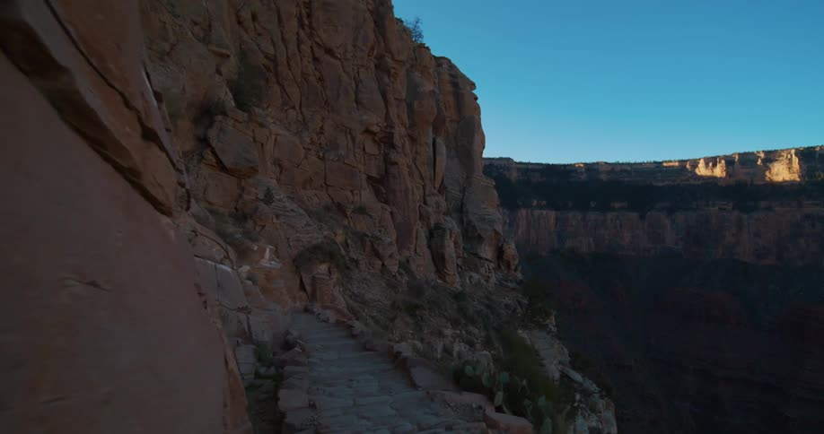 A stone step trail along a cliff ridge in a canyon under a bright blue sky