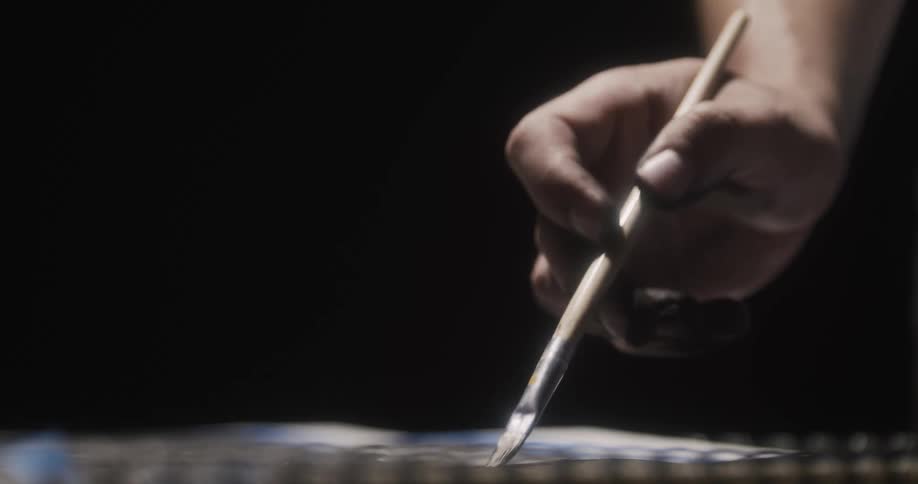 A persons hand painting a sketchbook with a painting brush