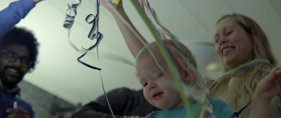 A young toddler and woman play with colorful balloon strings during a festive celebration.