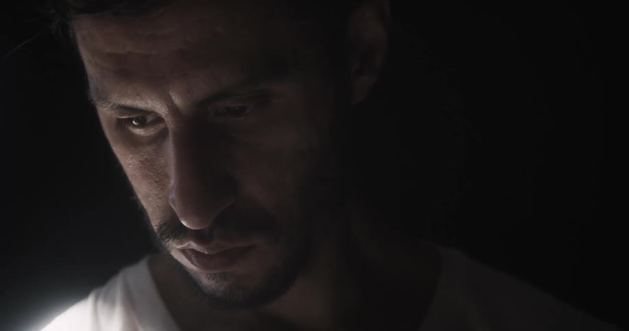 Bearded man focuses downward in dark area