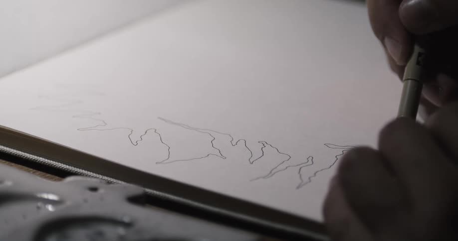 A man is sitting down at a table drawing with a black pen