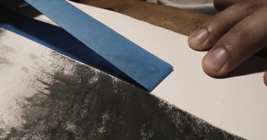 A man removes tape from a charcoal drawing