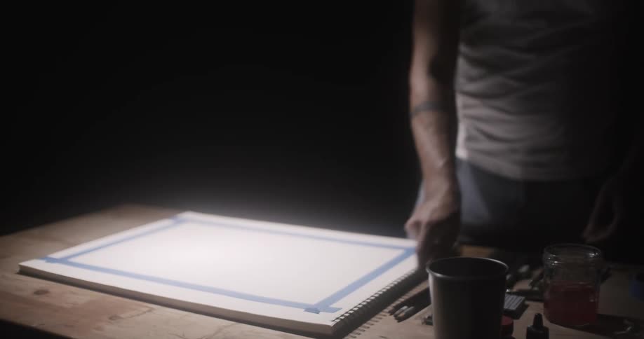 A man tapes down a piece of paper and picks up his pencil to sketch
