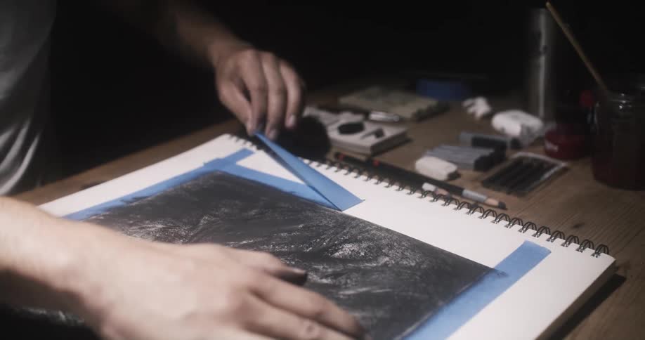 A person removes the tape from the artwork