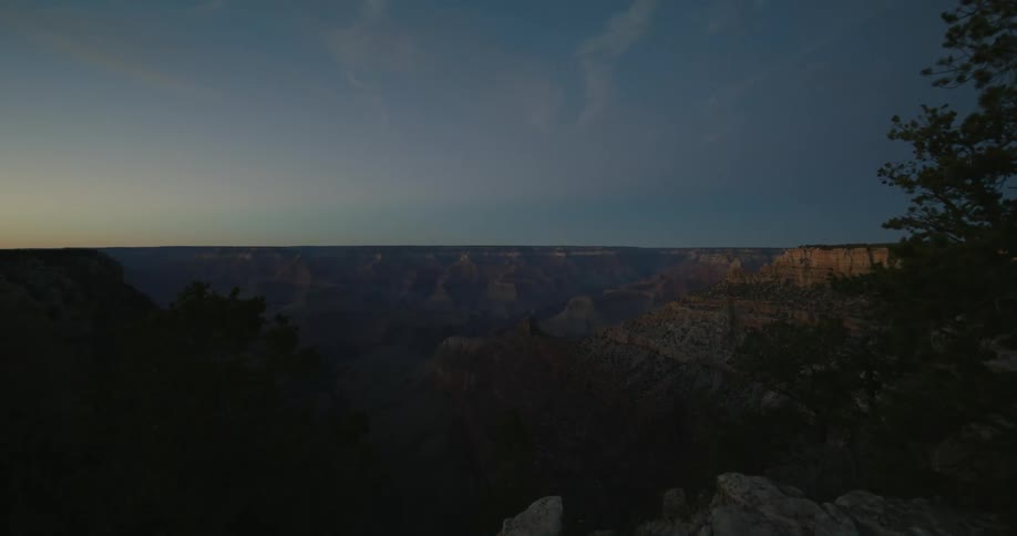 A man slowly approaches the edge of an immense canyon in the evening