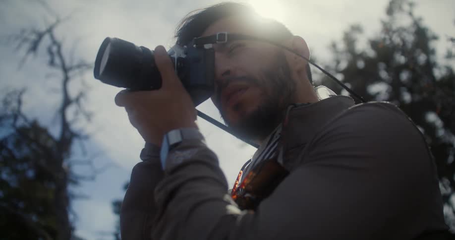 A man stands outside and picks up his camera and takes a photo