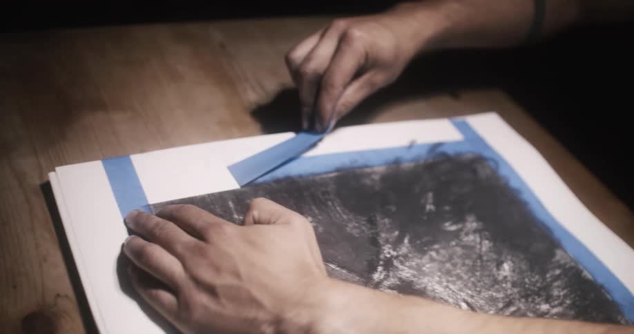 A man is pulling painters tape off a canvas