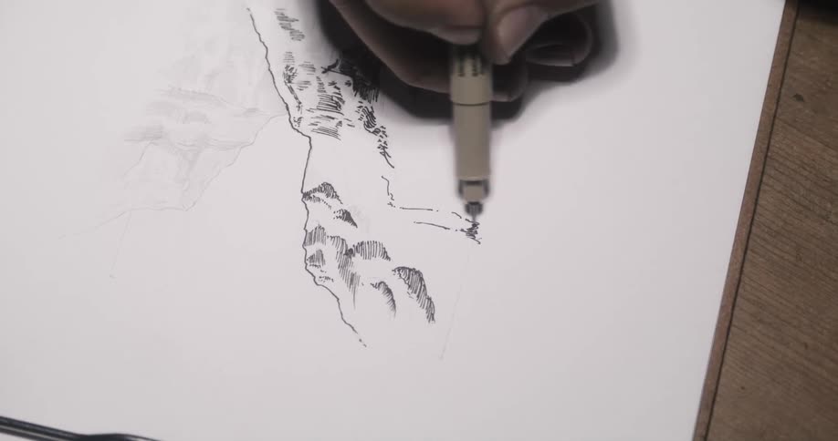 A man is sitting at a table drawing a picture with a black pen