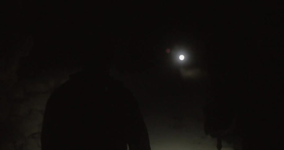 Two men are walking in the dark towards some lights