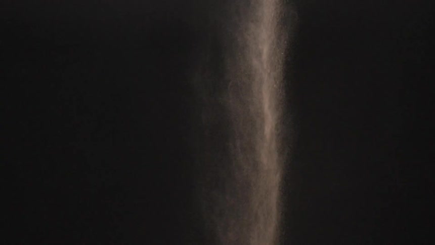 A gray powder is dumped into a dark room
