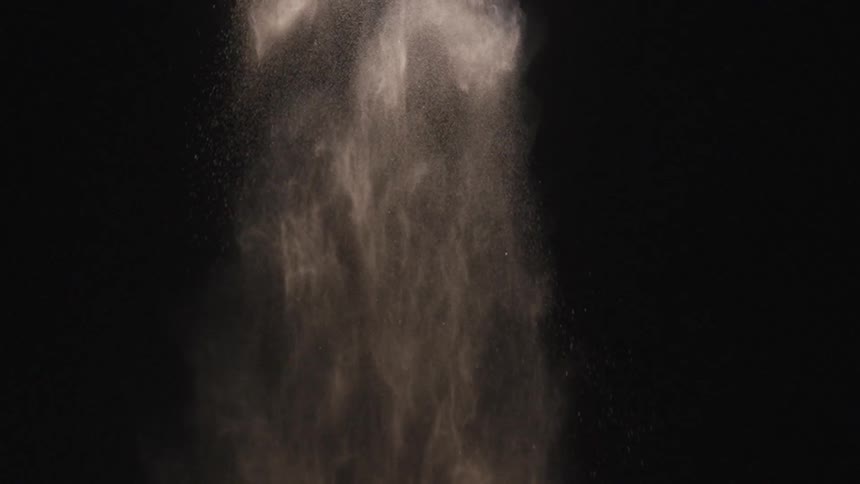 Gray powder falls slow and steady in a dark room