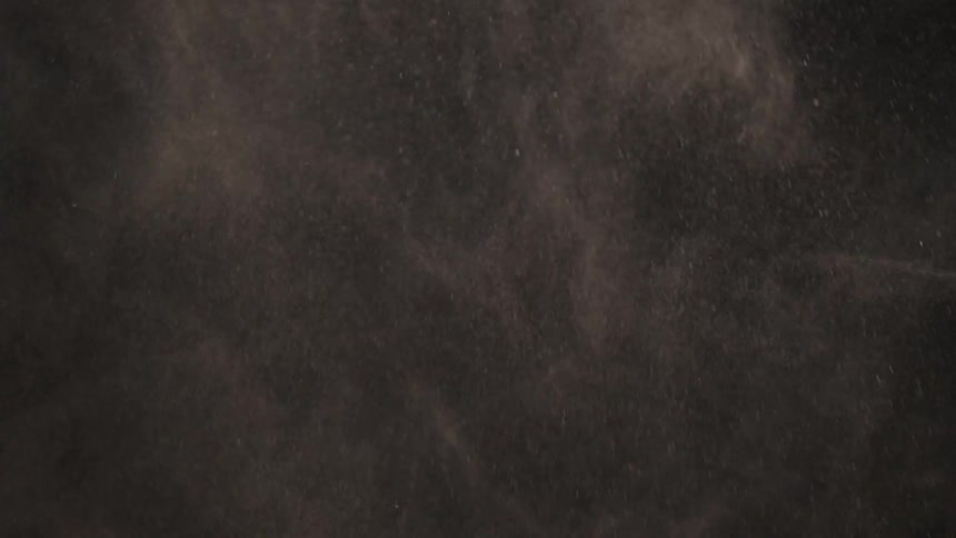 White particles swirl and fall as they dissipate against a black background