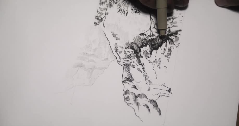 A man is sitting down at a table drawing a picture with a black pen