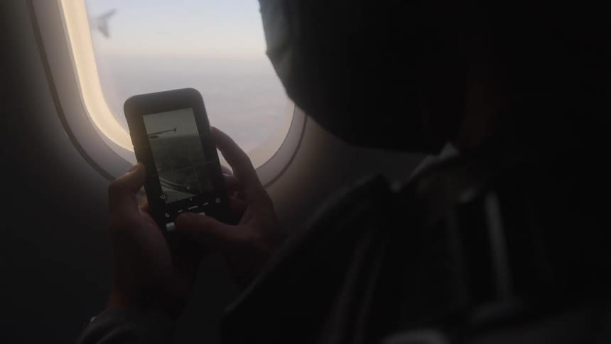 Airplane passenger wearing a face mask takes picture from the window using a cell phone