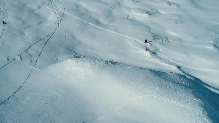 A person rides a snowmobile across hilly snow covered terrain during the day