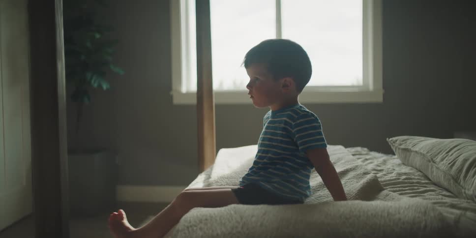 A little boy is sitting on his bed watching something with his full attention