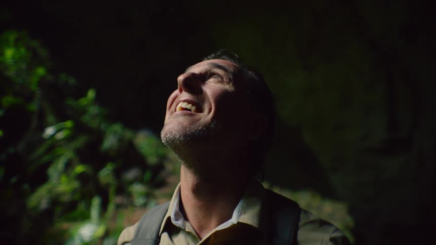 Sunlight is shining on a mans face as he looks around in the woods