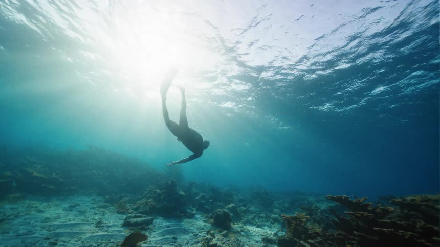 Silhouette of a person scuba diving in clear water as the sun shines above
