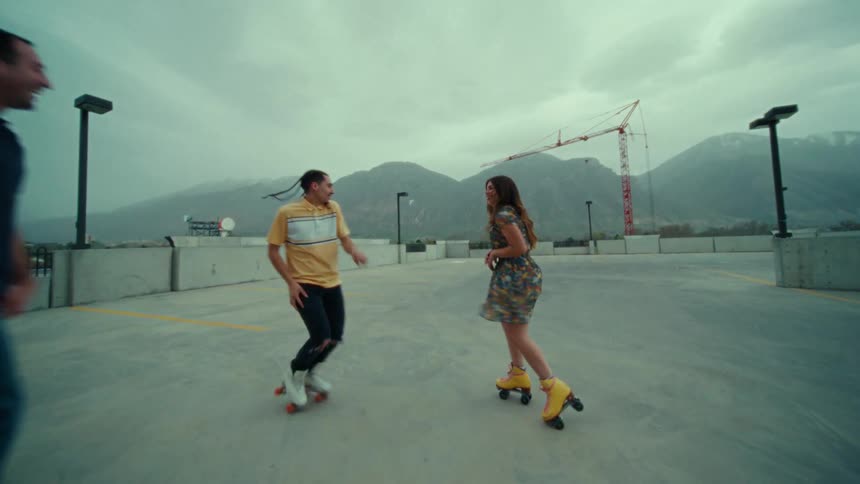 A group of people roller skate while dancing on the top floor of a parking garage on a cloudy day