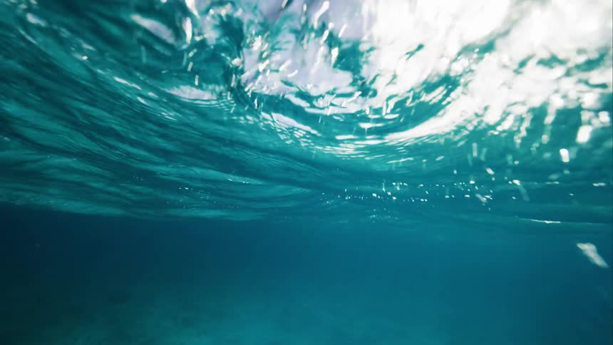 Underwater the sun is shining from above and breaking the surface the sky and clouds can be seen