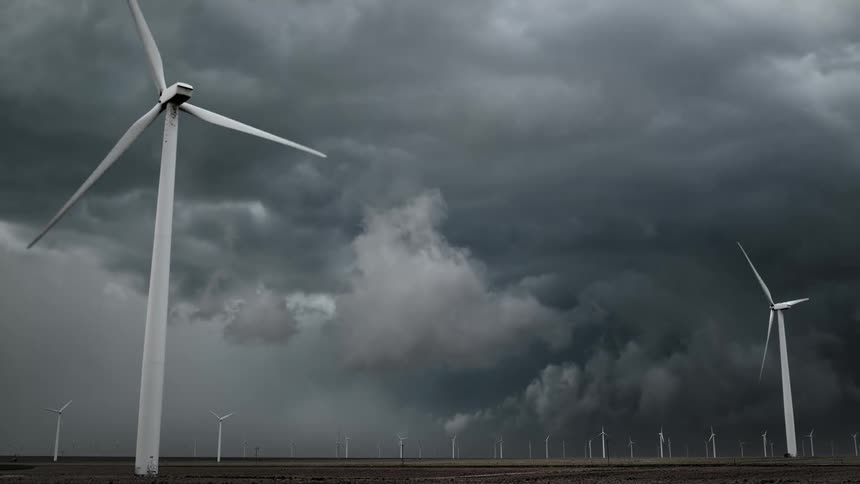 Wind turbines spin on a wind farm under a dark stormy sky with lightning in the air