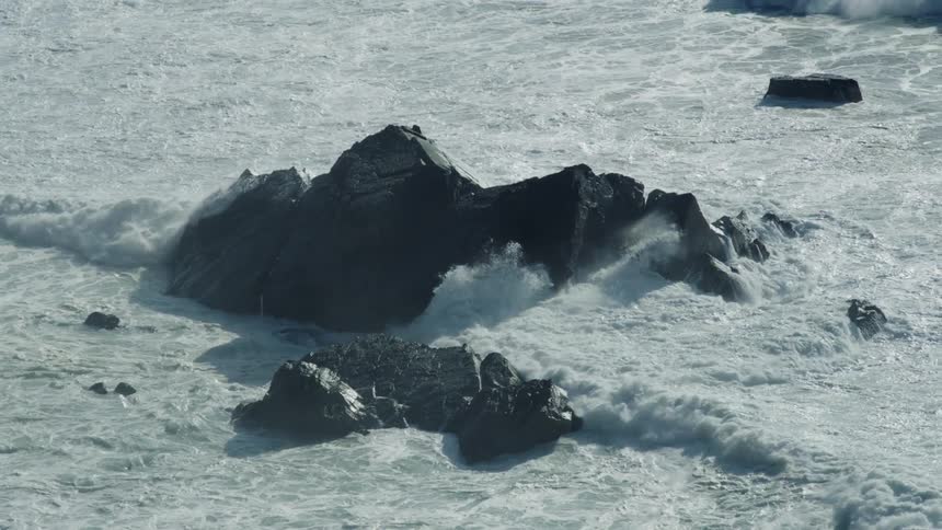 Waves are rolling into shore and crashing against rocks in the water