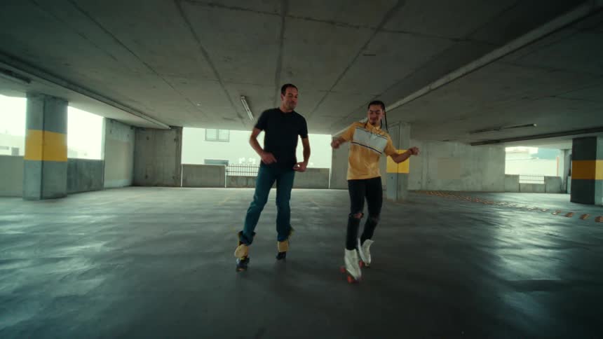 Two men dance on roller skates in a parking garage