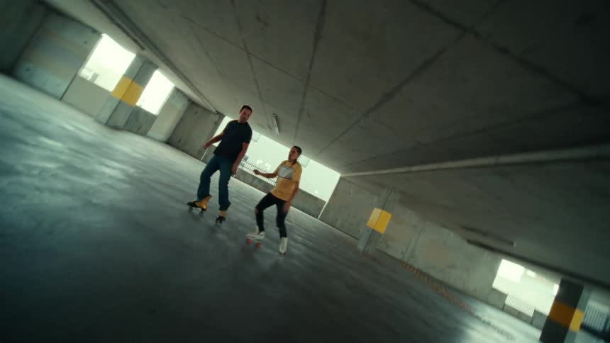 A pair of men dance while wearing rollers skates in a parking garage during the day