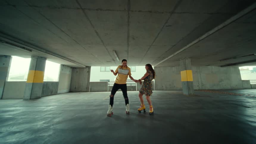 Man and woman dance on roller skates in parking garage