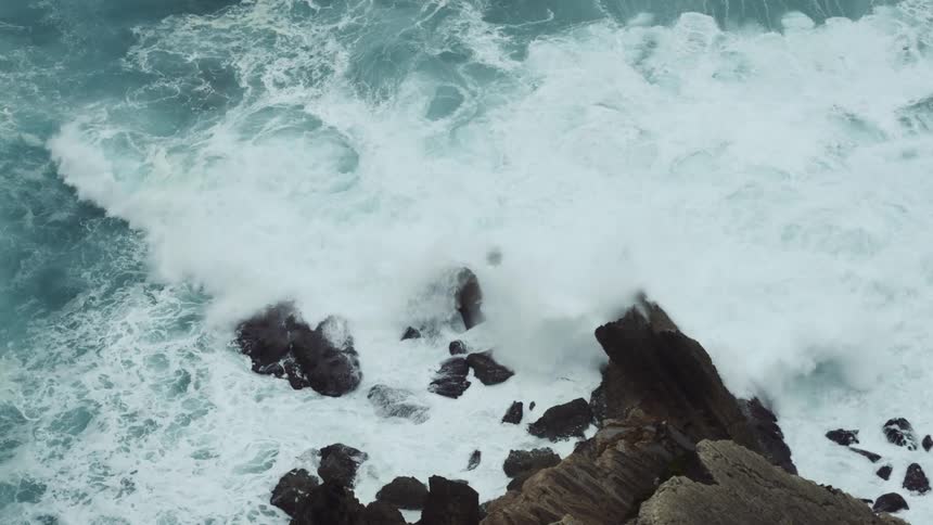 An ocean wave crashes into a rocky coastline during the day