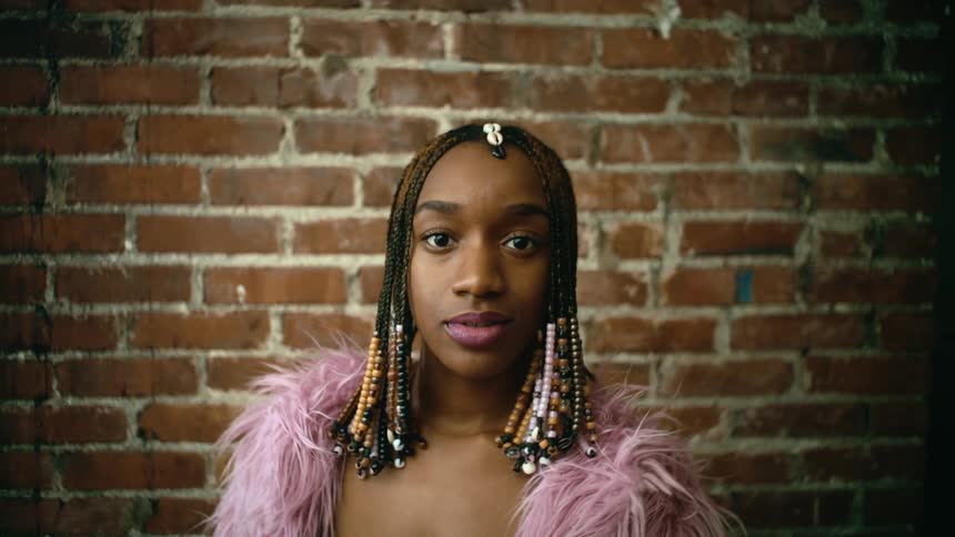 A young woman runs her hands through her braided hair while looking into the camera