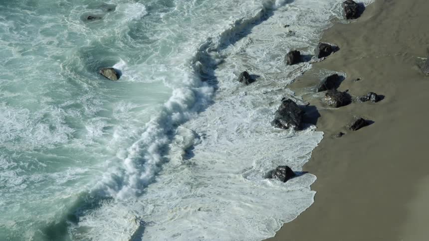 Ocean waves break over rocks on a sandy shore