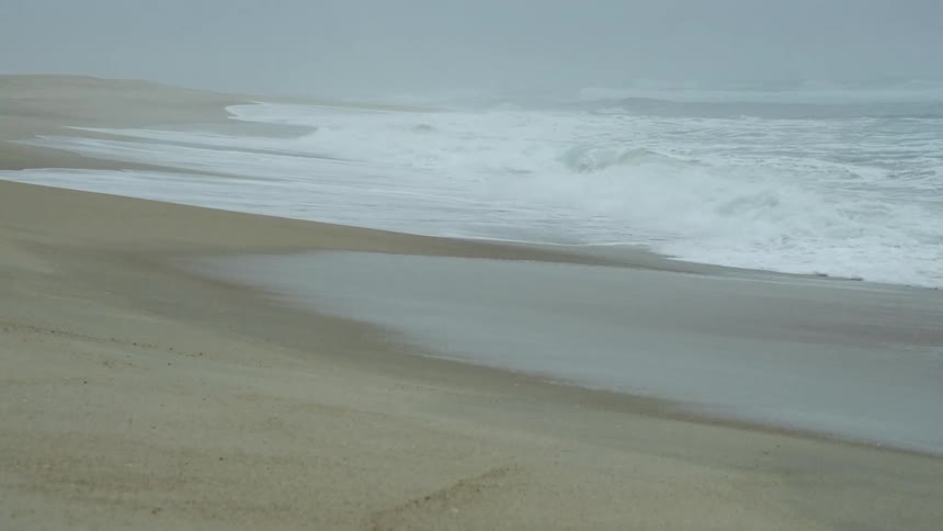 Waves roll into shore and over the sand on the beach