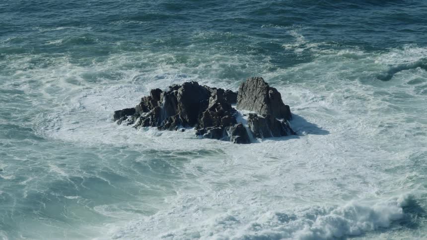Waves roll in and crash against rocks in the water and splash high in the air