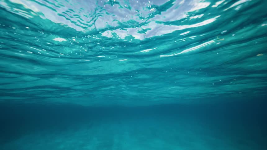 Underwater view of the sun shining from above and as the water wavers the sky and clouds can be seen