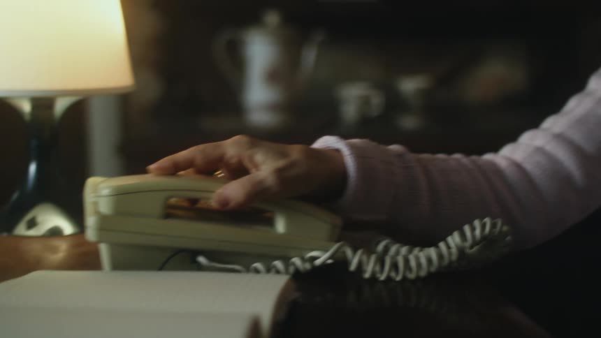 An elderly woman talks on a phone and then hangs up the receiver to the base