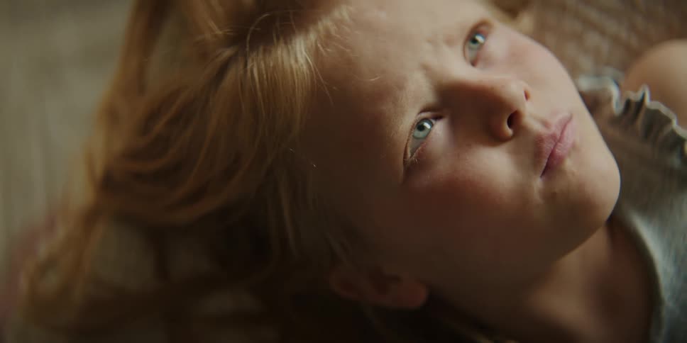 A redhaired girl lying down squinting a bit as she thinks