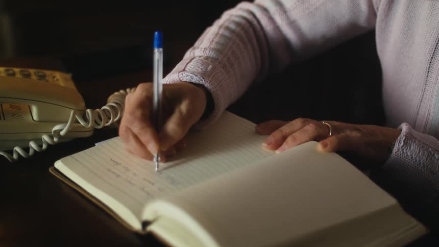 A woman sits at a desk and writes in a notebook