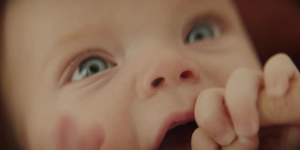 A baby happily puts its own fingers in its mouth and also grabs moms