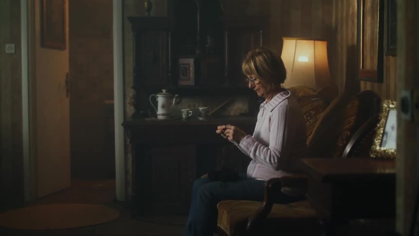 An elderly woman knits while sitting indoors in a house during the day
