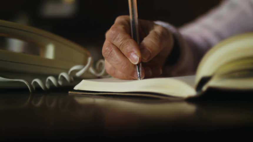 A woman is sitting at a table writing in a book