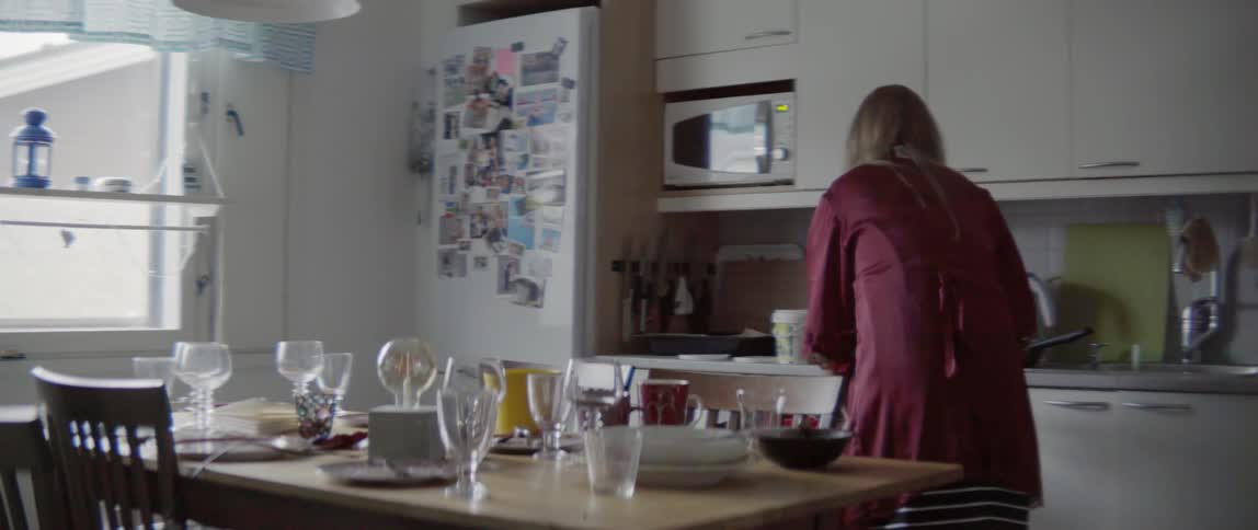 A woman walks into a kitchen and opens a dishwasher to put things in it