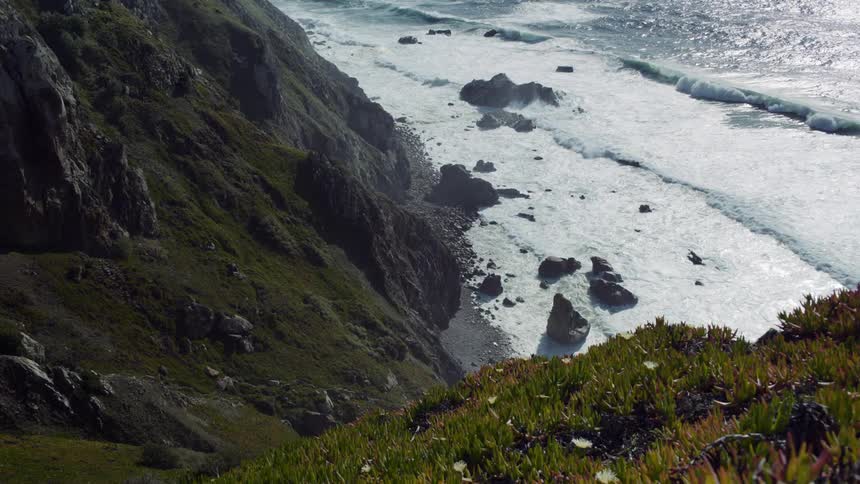 Waves roll into a rocky beach crashing up against the cliffs