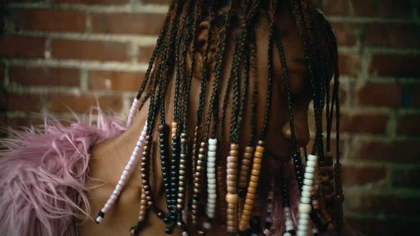 Woman with beaded hair braids turns her head to show her braids and smiles