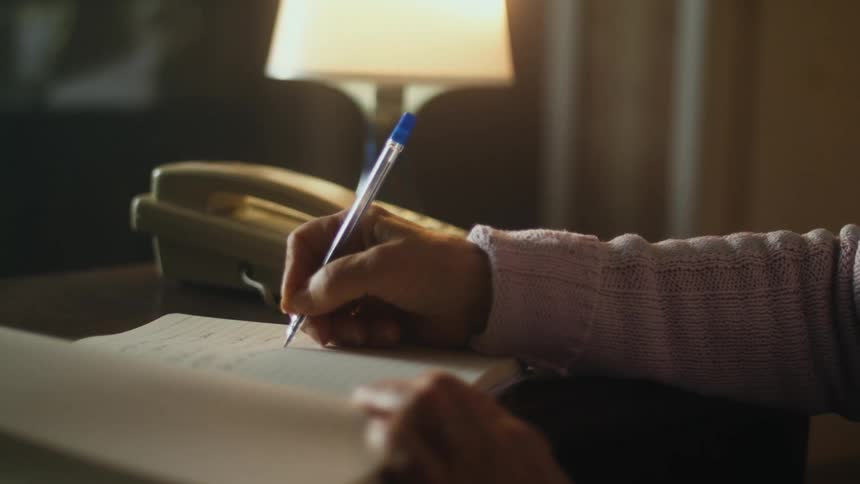 A person writes in a journal while sitting at a desk indoors