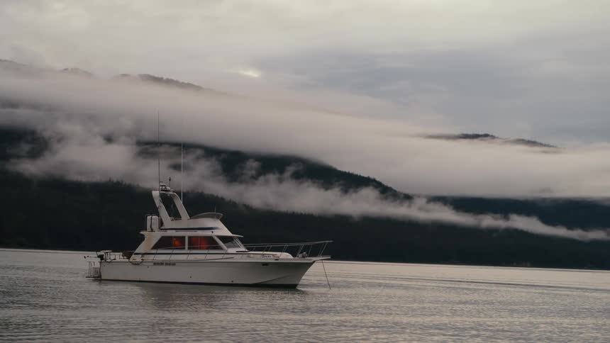 A boat is anchored on a calm body of water near a mountain as the sun goes down